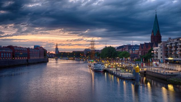Bremer Schlachte. Quelle: AdobeStock Fotos Zu sehen ist zentral der Fluss Weser. Dieser ist gerahmt von Gebäuden links und rechts. Die rechte Seite stellt den Beginn der Bremer Innenstadt dar, die Schlachte, die durch hohe Kaimauern und anliegenden alten Segelschiffen charakterisiert ist.