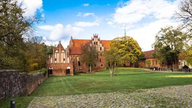 Kloster Chorin im Kreis Barnim. Quelle: Adobe Stock 178936616 Kloster mit grüner Wiese und vor blauem Himmel. Das Kloster ist aus roten Backsteinen.