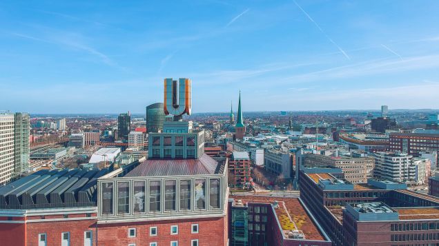 Zu sehen ist das Dortmunder U auf dem Dach eines hohen Gebäudes. Im Hintergrund erstreckt sich die Stadt Dortmund aus Vogelperspektive.