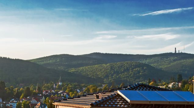 Hinter einem Hausdach mit solaranlagen erstreckt sich der Taunus: Mittelgebirge mit bewaldeten Hügeln.