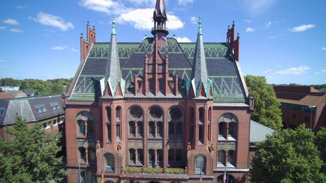 Altes Rathaus der Stadt Neumünster. Quelle: Julia Schirrmacher und Luise Hannink Zu sehen ist ein großes, altes Backsteingebäude. Die Fassade ist durch Türmchen und große Fenster aufgewertet. es handelt sich um das alte Rathaus der Stadt Neumünster.