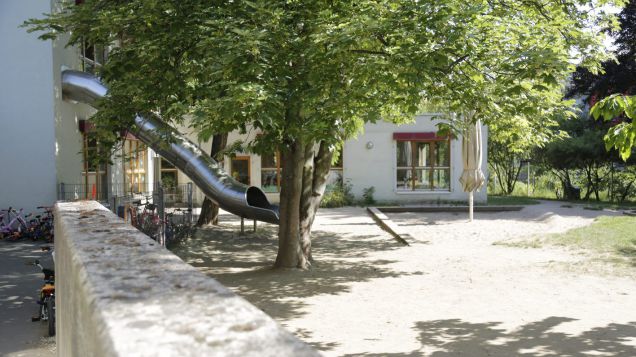 Außenbereich der Kita mit Baum, Rutsche und Sandkasten.