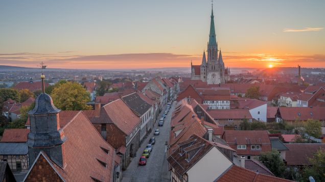 Zu sehen ist eine altertümliche Stadt mit Kirchturm bei Sonnenuntergang.