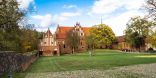 Kloster mit grüner Wiese und vor blauem Himmel. Das Kloster ist aus roten Backsteinen.