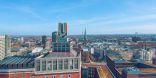 Zu sehen ist das Dortmunder U auf dem Dach eines hohen Gebäudes. Im Hintergrund erstreckt sich die Stadt Dortmund aus Vogelperspektive.