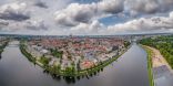 Zu sehen ist die Stadt Lübeck aus Vogelperspektive. Ein Fluß umrahmt die Innenstadt. Diese besteht aus vielen roten backsteinhäusern. Das Bild ist im Weitwinkel aufgenommen.
