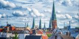 Dächer der Stadt Oldenburg. Zu sehen ist ein hoher Turm mit türkisenem Spitzdach. Dieser ist umgeben von weiteren Stadthäusern.
