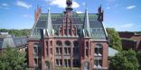 Zu sehen ist ein großes, altes Backsteingebäude. Die Fassade ist durch Türmchen und große Fenster aufgewertet. es handelt sich um das alte Rathaus der Stadt Neumünster.