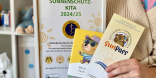 Person hält Bilderrahmen und zwei Prospekte in der Hand.