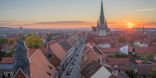 Zu sehen ist eine altertümliche Stadt mit Kirchturm bei Sonnenuntergang.