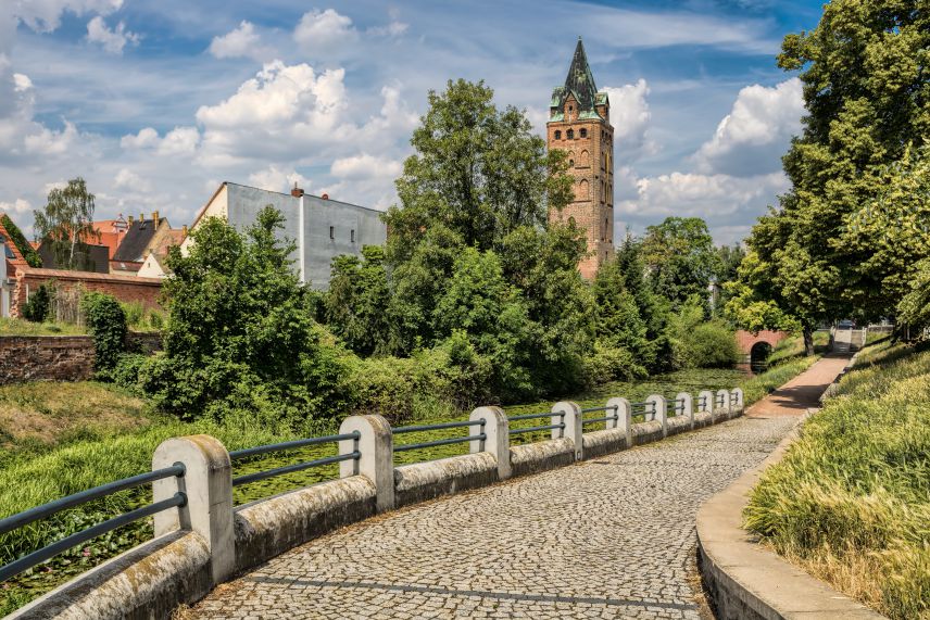 Gewundene Straße mit Kopfsteinpflaster, daneben viel Grün und im Hintergrund ein historisches Gebäude.
