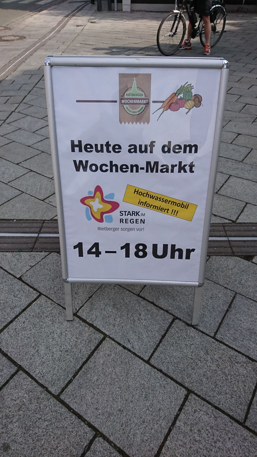Foto von einem Aufsteller, der auf ein Informationsangebot zum Hochwasserschutz auf dem Rietberger Wochenmarkt hinweist