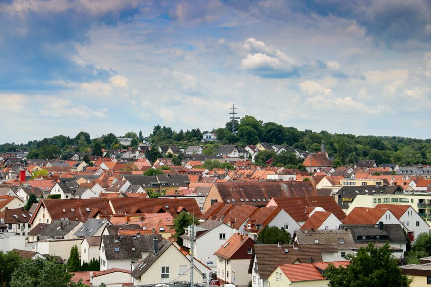 Stadtansicht Dietzenbach mit Aussichtsturm. Quelle: Kreisstadt Dietzenbach Zu sehen ist aus Vogelperspektive die Dächer einer Stadt. Im Hintergrund ist ein Aussichtsturm im Wald zu sehen.