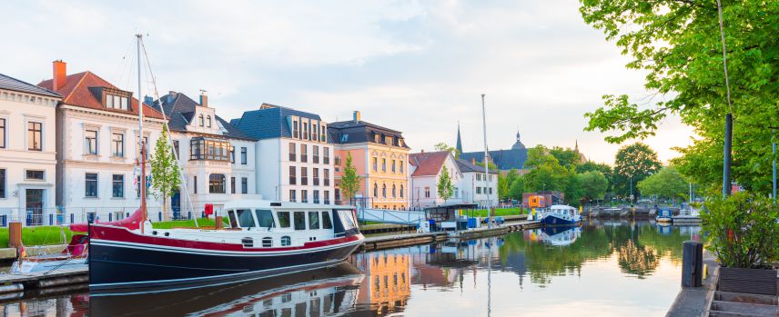 Kanal mir Häusern daran. Auf dem Kanal ist ein Boot. Im Hintegrund sieht man noch mehr Teile der Stadt.