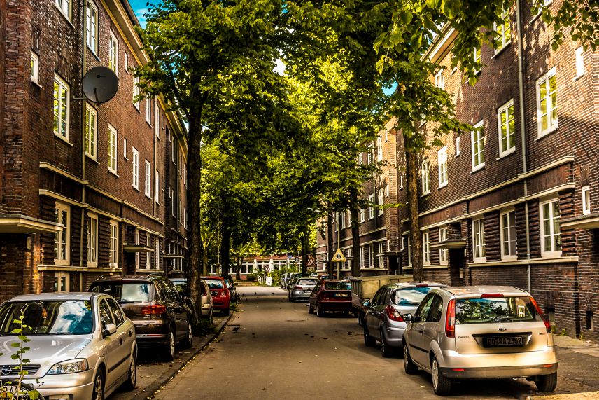 Dortmunder Nordstadt. Quelle: AdobeStock Fotos Zu sehen ist eine Straße gesäumt von Häusern links und rechts. Die Häuser sind aus einem dunklen Backstein. Vor den Häusern parken Autos und Bäume säumen die Straße.