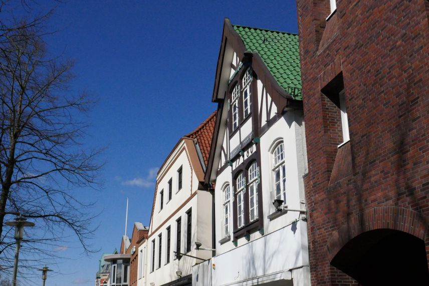 Zu sehen sind die Fassaden von 3 größeren Gebäuden. im Hintergrund ist blauer Himmel zu sehen.