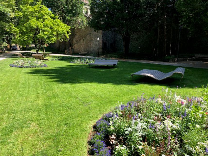 Bänke im Zwingerpark zum kühlenden Aufenthalt an heißen Tagen. Quelle: Stadt Offenburg Park mit angelegter Rasenfläche und Liegebänken aus Holz, die im Baumschatten stehen.
