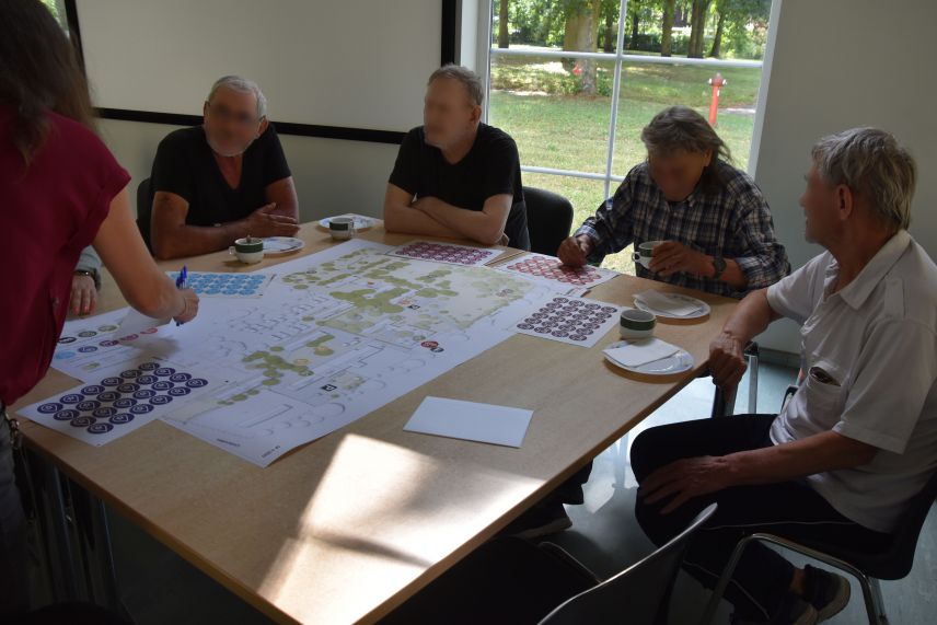 Beteiligungsprozess während der Arbeit am Konzept. Quelle: AWO Bezirksverband Potsdam e.V. Menschen sitzen vor einem Plan rund um einen Tisch und sind ins Gespräch vertieft.