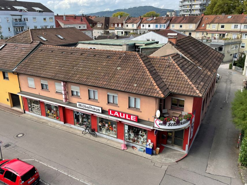 Zu sehen ist ein Eckhaus mit zwei Stockwerken. Im Erdgeschoss sind Schaufenster. Es hängen Schilder an der Fassade auf denen steht "Möbel", "Möbelhaus" und "Laule". Über der Eingangstür hängt ein Schild, auf dem steht "AWO Schatzkästlein".