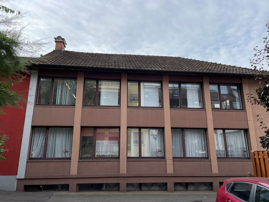 Zu sehen ist die Fensterseite eines braunen Hauses mit zwei Stockwerken.